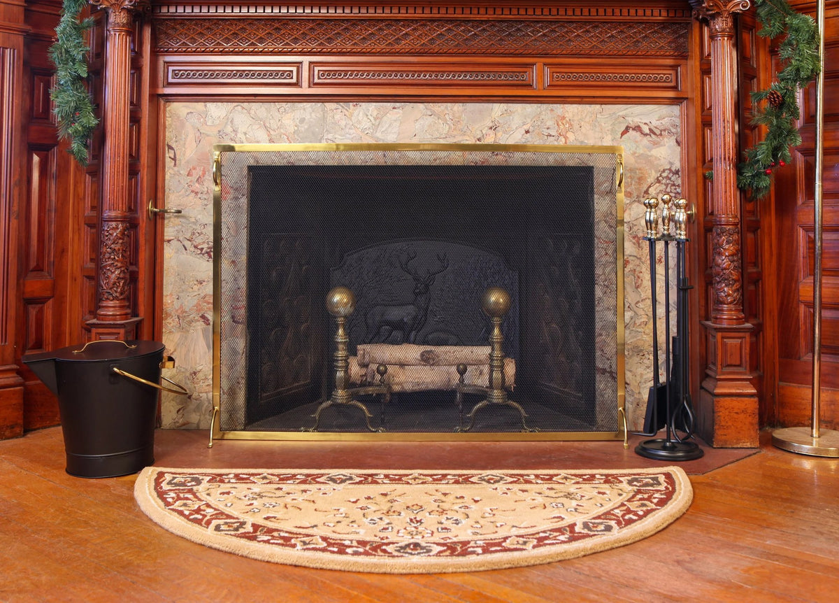 Montreal screen in polished brass at a panelled fireplace with andirons and a coal hoop