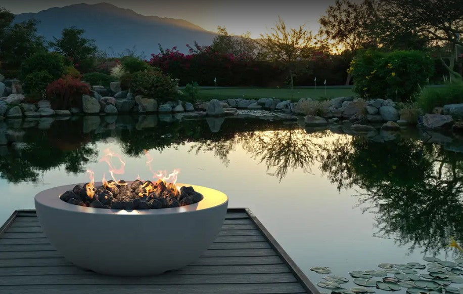 Round concrete gas fire bowl lit on a lakeside deck at dusk