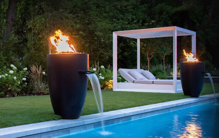 Tall concrete fire and water vases lit beside a pool
