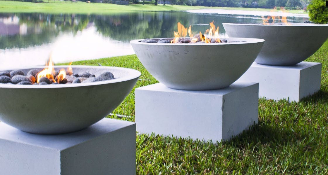 Concrete gas fire bowls on plinths beside a lake