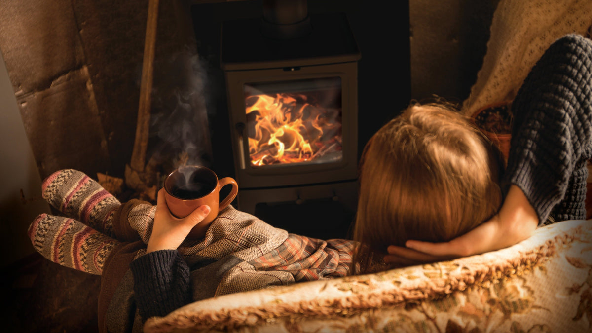A wood burning stove alight in a stone hearth, seen from a sofa